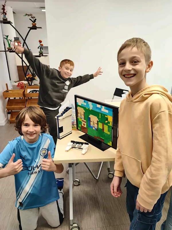 Trois membres du club, pouces levés, devant une télévision et une manette réalisées en briques LEGO®