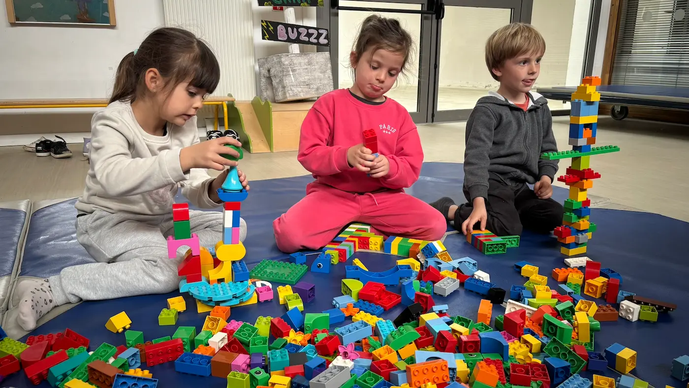 Hub collectivités 9 20/10/2026 Animation d'accueil de loisirs à Pélissanne : trois jeunes enfants construisent une haute tour en briques DUPLO® sur un tapis