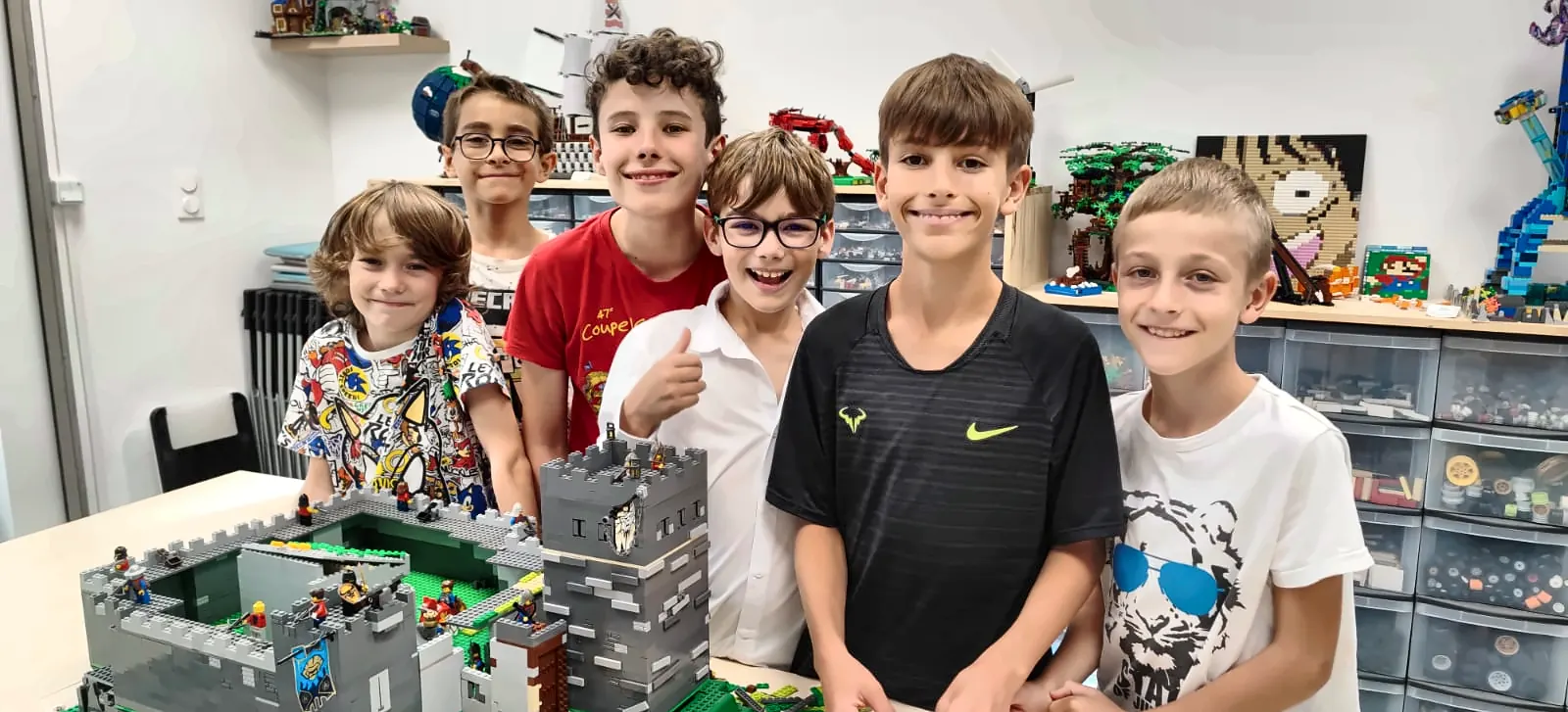 Six enfants posent en souriant devant un château fort en briques LEGO® qu'ils viennent de construire, pendant un anniversaire dans l'espace créatif de Ludi Briques à Salon-de-Provence