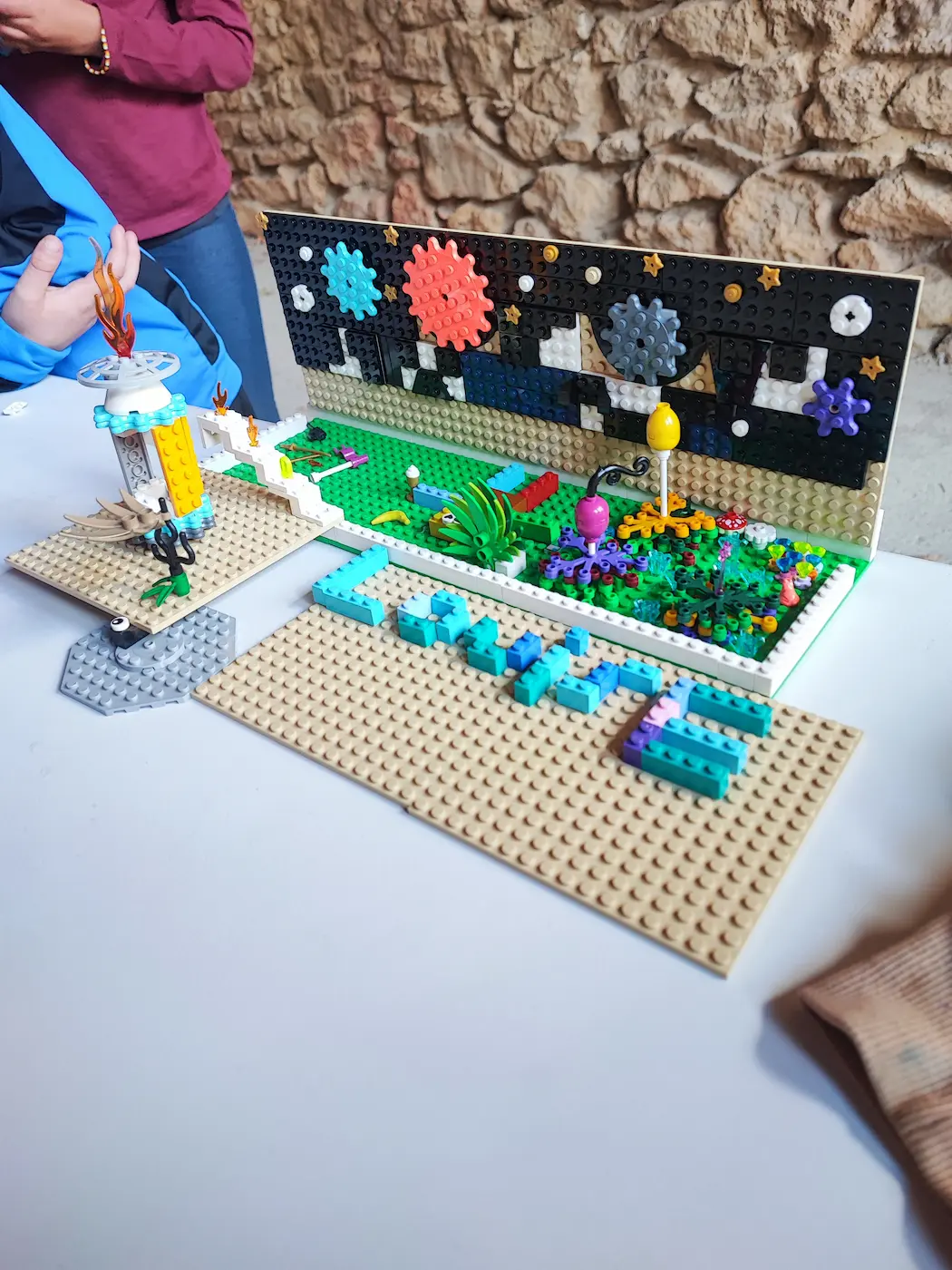 Centres de loisirs 7 21/10/2026 Animation centre aéré à Miramas : un décor créé par des enfants en briques LEGO®, avec un jardin fleuri, un feu d'artifice et des engrenages