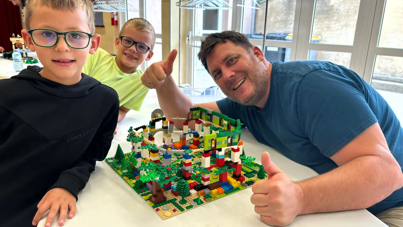 Hub collectivités 1 20/10/2026 Animation originale pour collectivités : un adulte et deux enfants lèvent le pouce devant leur jardin construit en briques LEGO® lors d'une fête locale