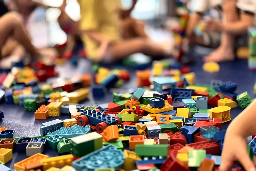 Animation anniversaire enfant Pitchouns, 3 à 5 ans : des enfants assis par terre construisent avec de grosses briques DUPLO® colorées, éparpillées au premier plan