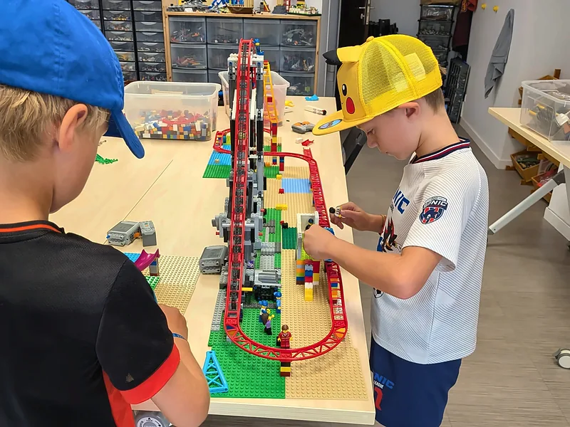 Deux membres du club construisent une montagne russe en briques LEGO® sur une longue table, au club de Salon-de-Provence