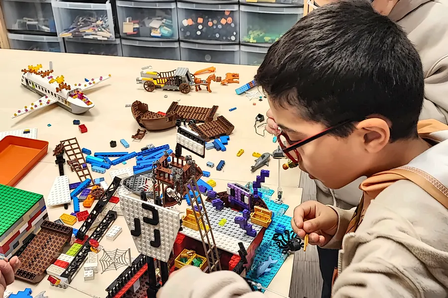 Un enfant assemble un bateau pirate en briques LEGO® pendant son anniversaire dans l'espace créatif de Salon-de-Provence, devant les tiroirs de pièces triées