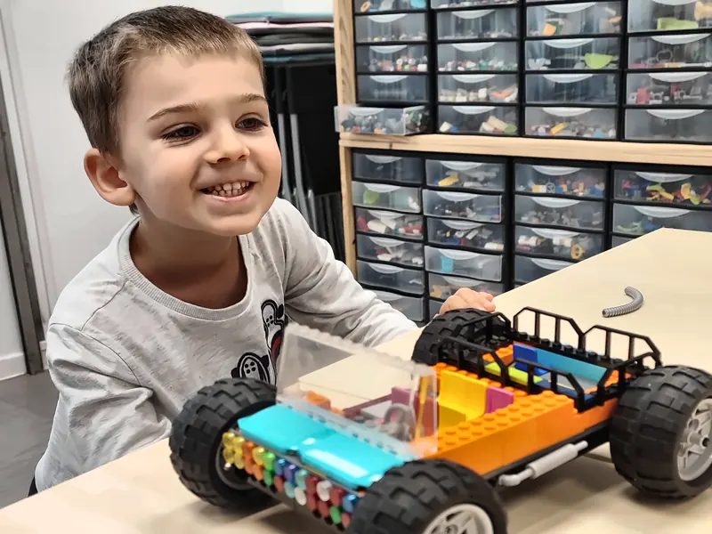 Enfant souriant devant sa voiture tout-terrain en briques LEGO® Technic, construite en accès libre dans la salle de jeux de Salon-de-Provence