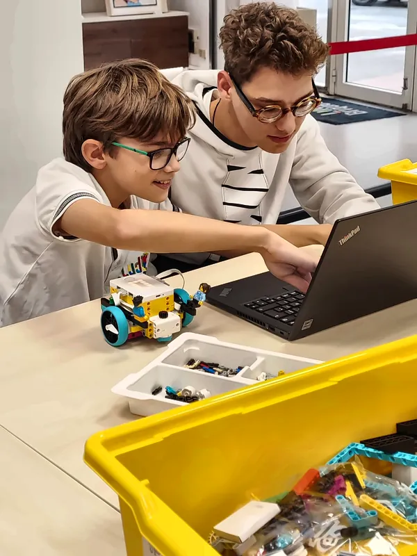 Deux membres du club robotique, un enfant et un ado, programment ensemble un petit robot sur un ordinateur portable