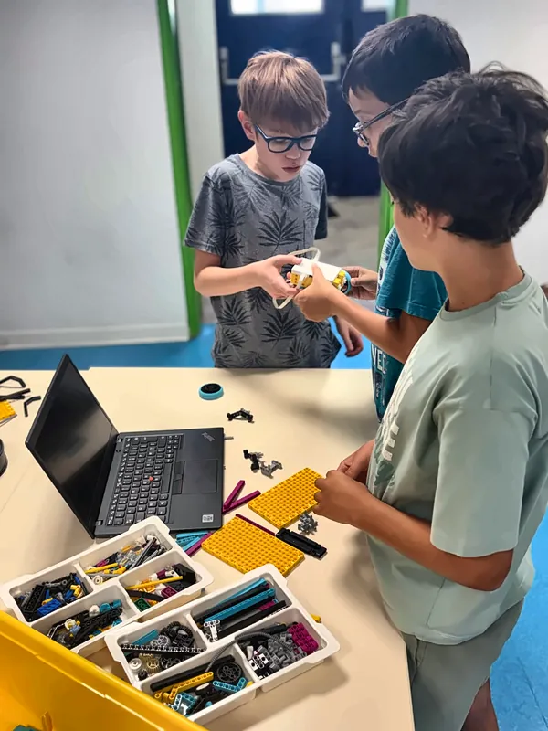 Trois jeunes membres du club robotique préparent un robot ensemble, avec un ordinateur et des bacs de pièces