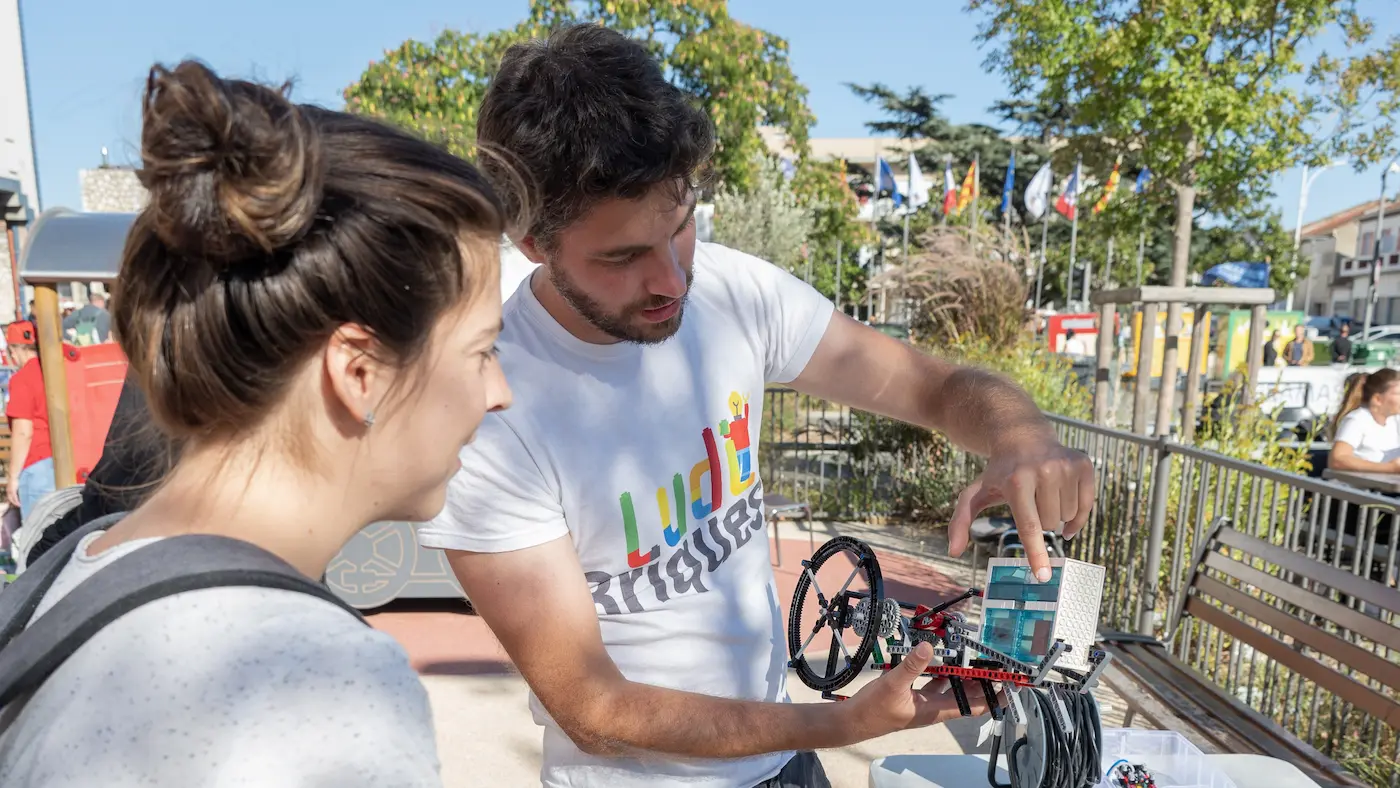 Hub collectivités 5 20/10/2026 Animation originale à la fête du train de Miramas : un Expert Briqueur, encadrant constructeur, montre un mécanisme en briques LEGO® à une visiteuse