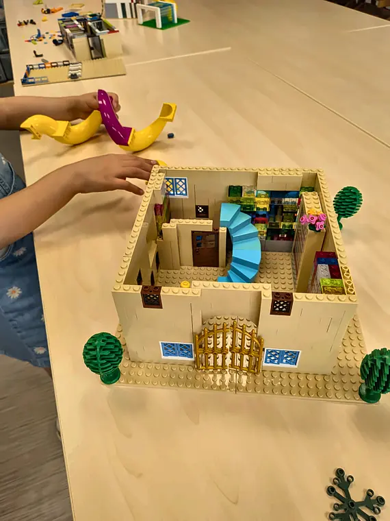 Accès libre 12 20/10/2026 Maison beige en briques LEGO® avec escalier bleu, grille dorée et toboggan jaune, construite par un enfant en accès libre