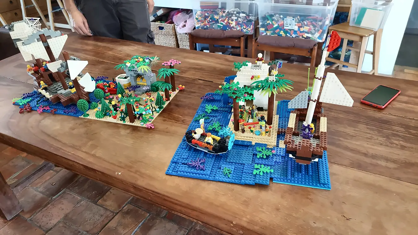 Deux îles pirates en briques LEGO® posées sur une table en bois, avec galion, palmiers et mer bleue, créées pendant un anniversaire à domicile