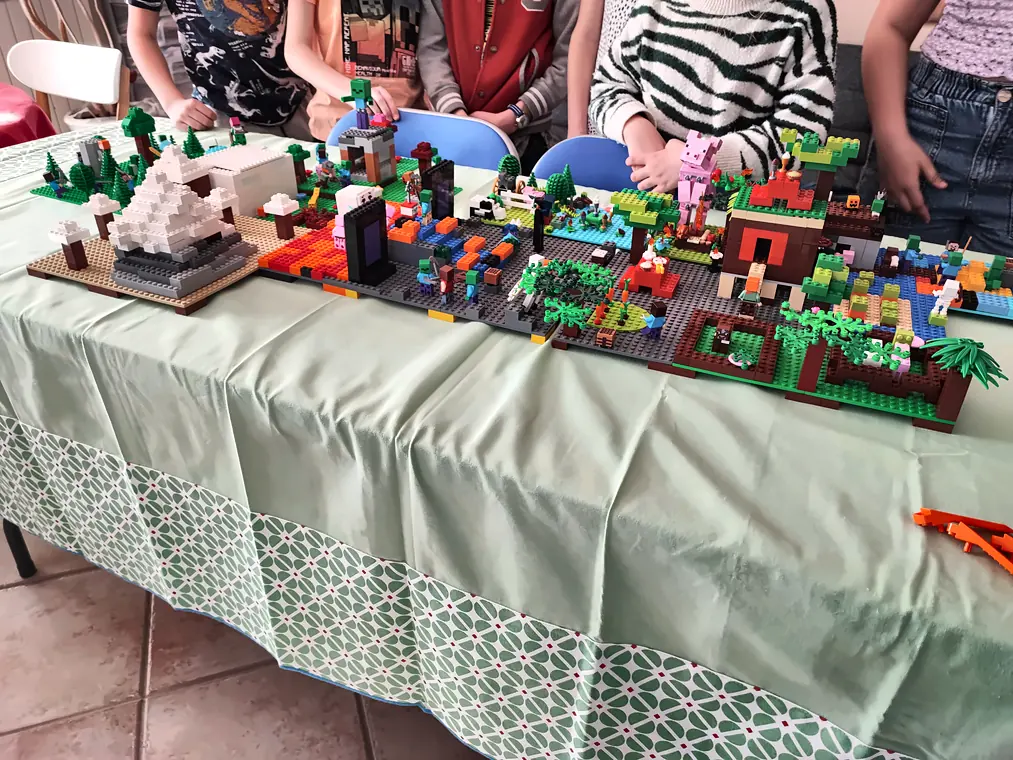 Table d'exposition des créations d'anniversaire : pyramide, jungle, maisons et villes en briques LEGO® alignées devant les enfants