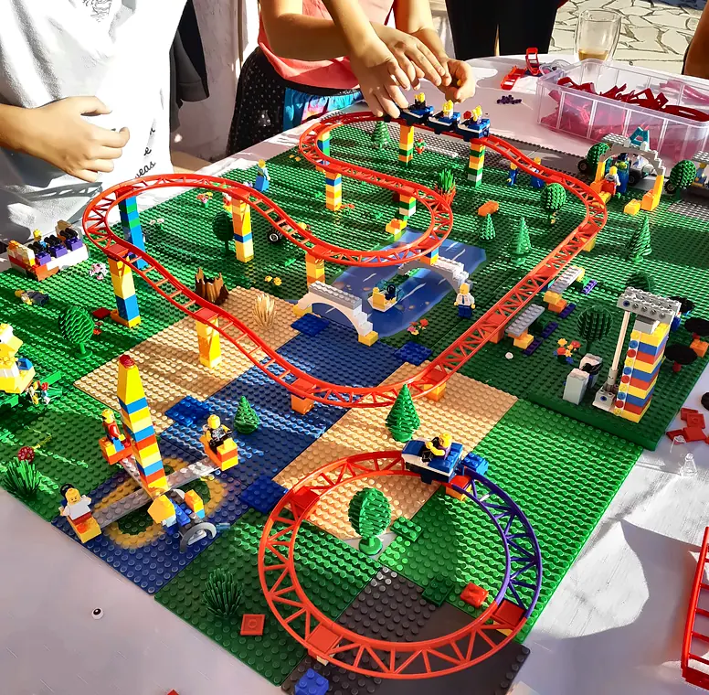 Montagne russe rouge en briques LEGO® avec village et plaques vertes, vue du dessus, construite à plusieurs pendant un anniversaire