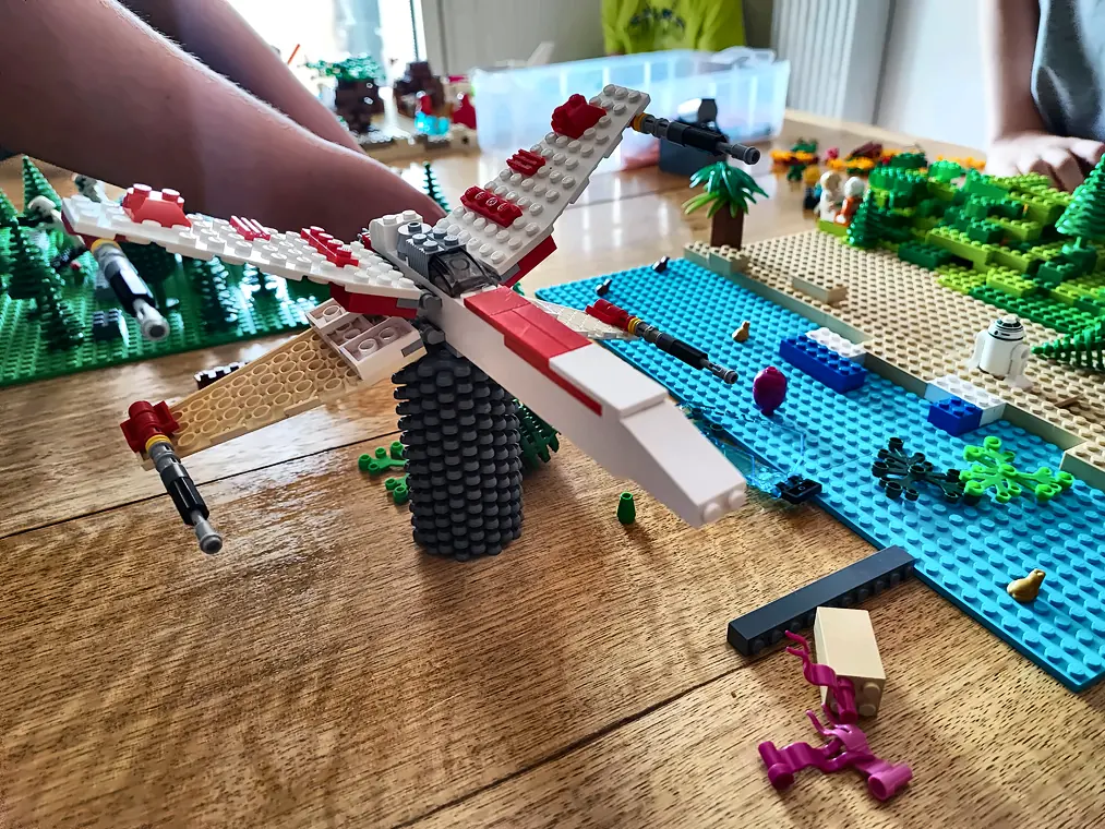 Grand vaisseau spatial blanc et rouge en briques LEGO® au-dessus d'une rivière turquoise, construit par un enfant pendant un anniversaire
