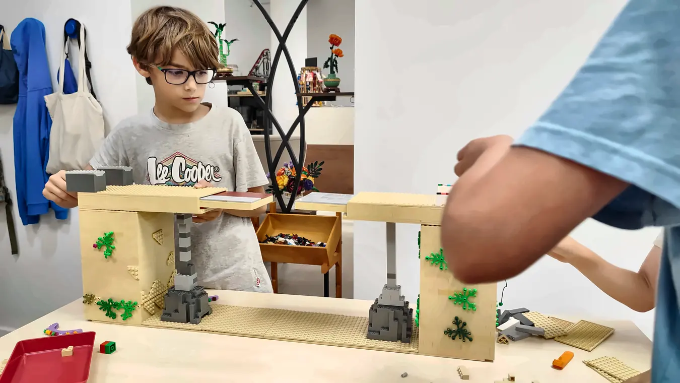 Stage vacances 19 20/10/2026 Participant concentré, lunettes sur le nez, qui teste un pont solide et rétractable en briques LEGO® posé entre deux piliers, un défi de construction façon LEGO® Masters