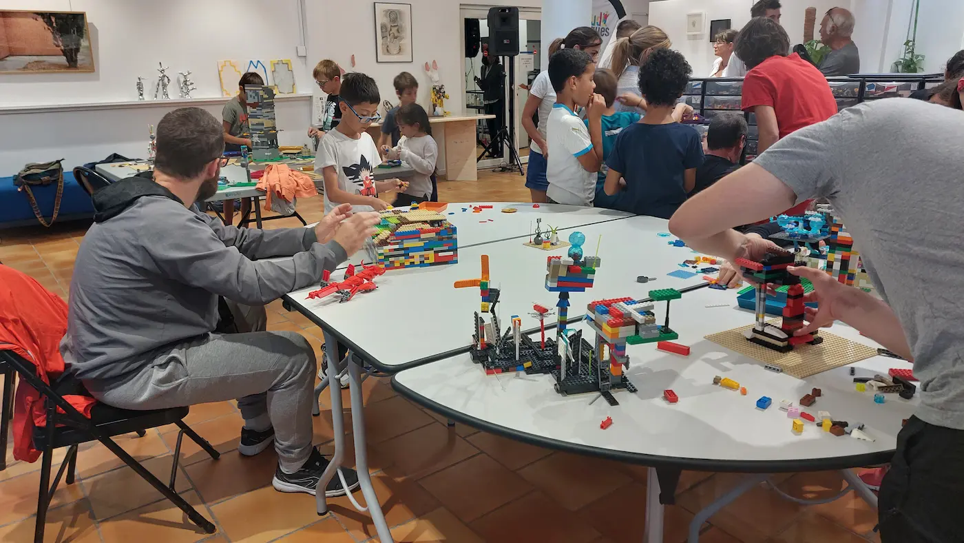 Sous-Hub Événement entreprise 2 20/10/2026 Événement entreprise en famille : adultes et enfants assemblent des constructions en briques LEGO® autour de tables rondes