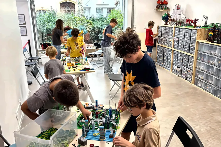 Participants d'un stage vacances scolaires qui construisent ensemble une ville en briques LEGO®, près des tiroirs de pièces triées du centre de créativité de Salon-de-Provence