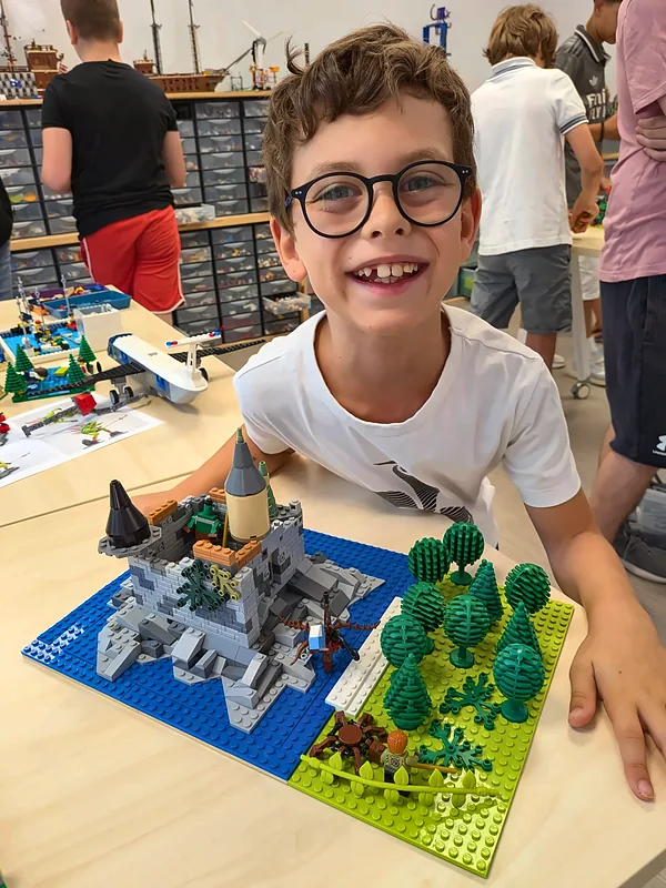 Jeune membre souriant devant son château en briques LEGO®, dans l'atelier du club de construction de Salon-de-Provence