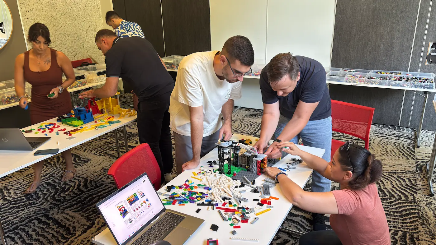 Séminaires 5 20/10/2026 Activité séminaire CODIR : des participants assemblent ensemble une construction en briques LEGO® autour d'une table, avec un ordinateur portable ouvert