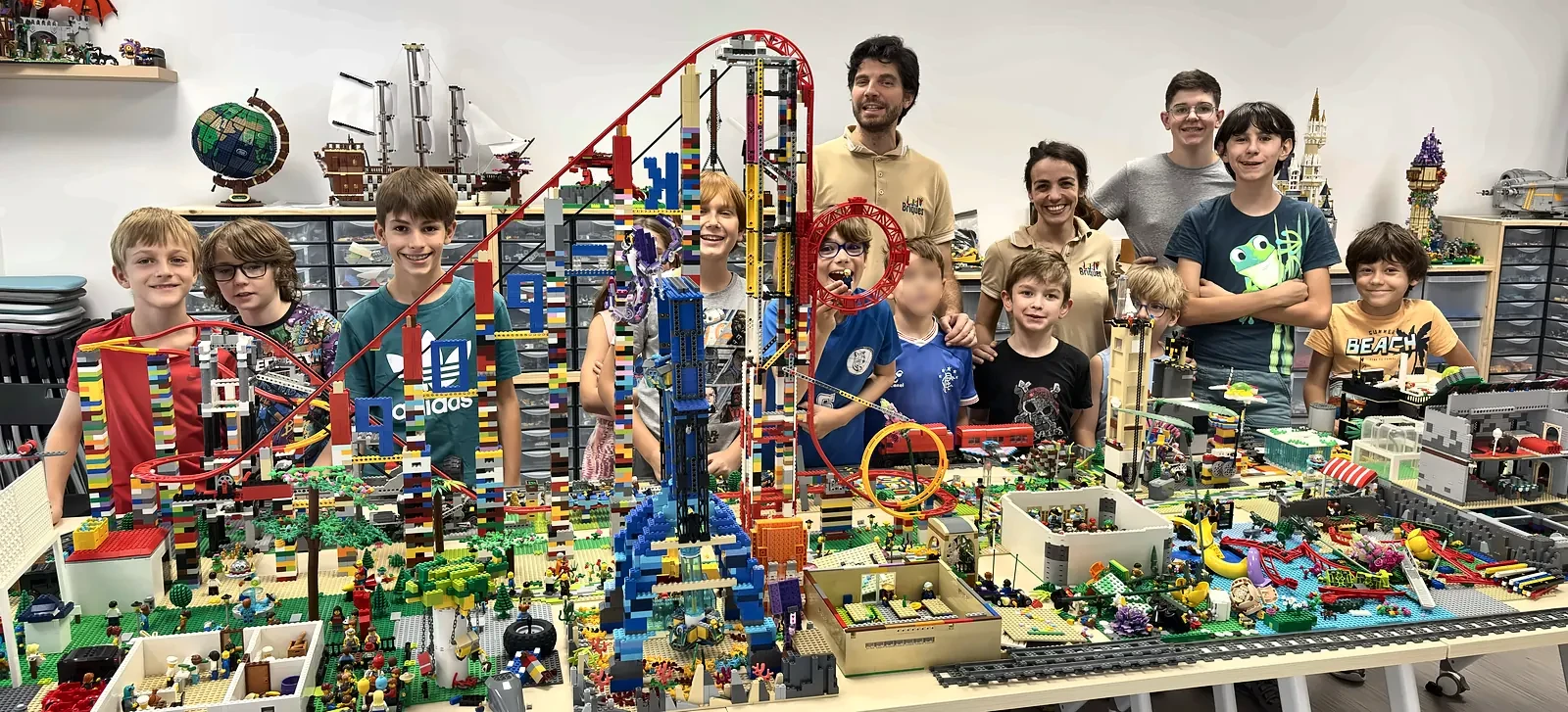 Accueil 3 20/10/2026 Une équipe de participants et d'encadrants pose devant un parc d'attractions avec montagne russe motorisée, construit en briques LEGO®