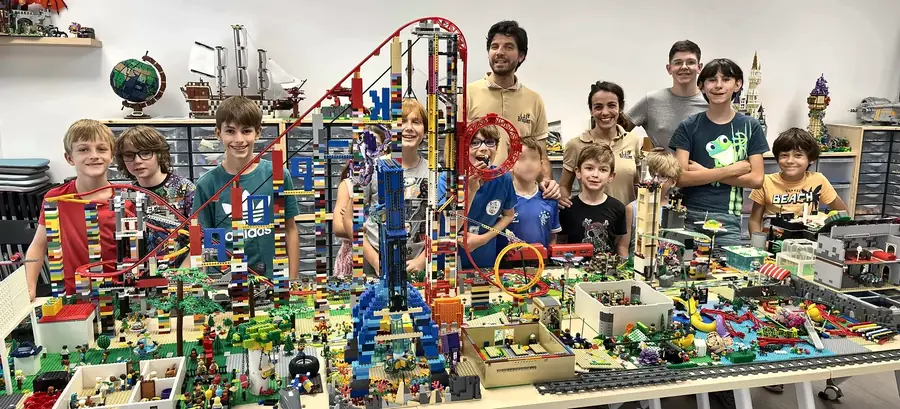 Une équipe de participants et d'encadrants pose devant un parc d'attractions avec montagne russe motorisée, construit en briques LEGO®