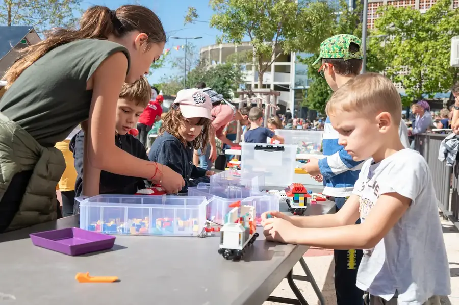 Enfants et parents construisent en briques LEGO® autour d'un stand de bacs de pièces, lors d'un événement en plein air