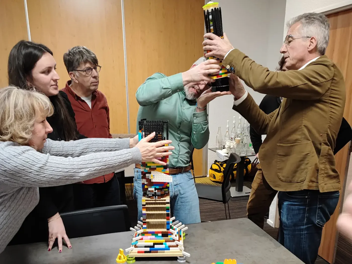 Séminaires 2 20/10/2026 Activité séminaire : des participants soutiennent ensemble une haute tour en briques LEGO® posée sur une table de réunion