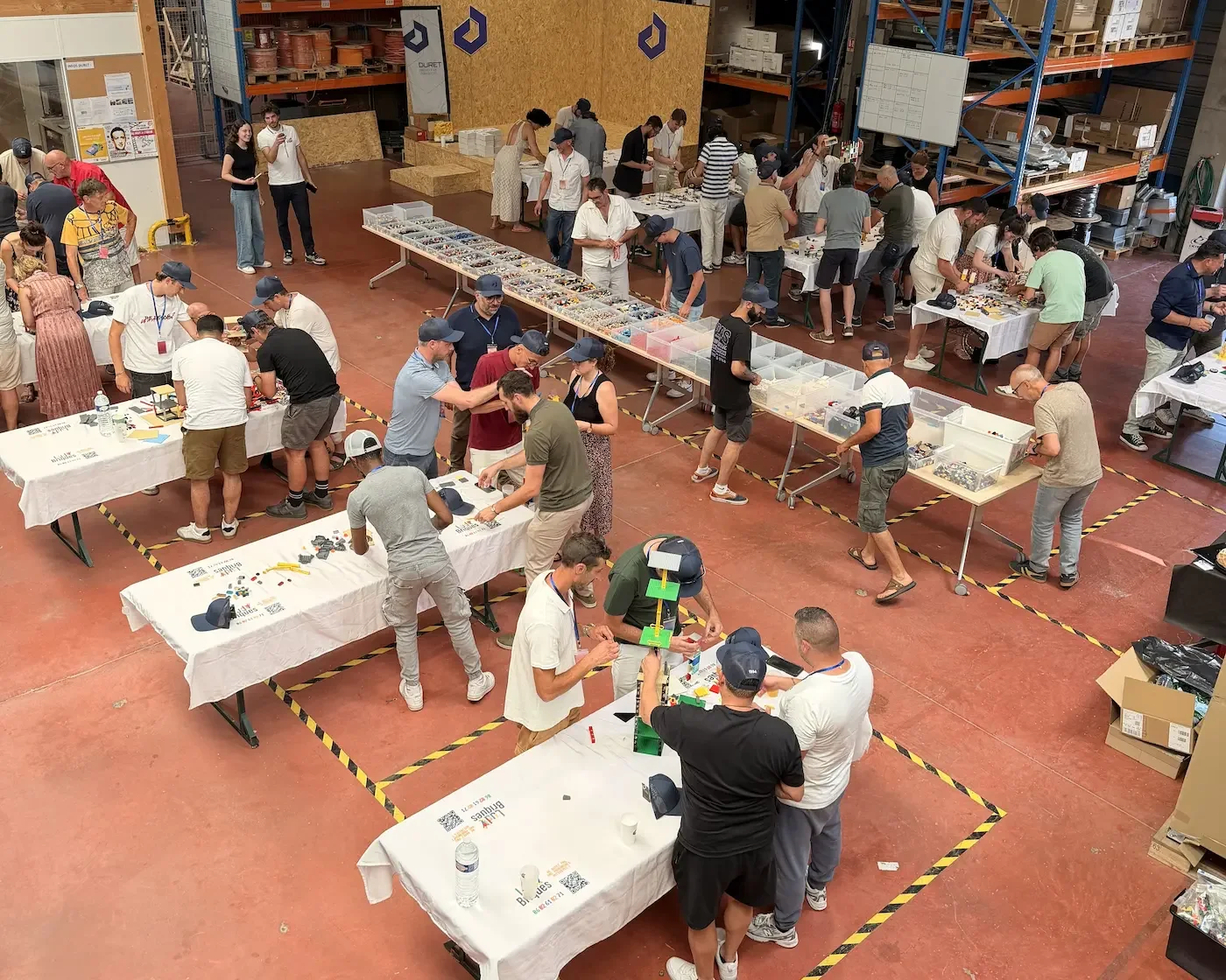 Accueil 4 20/10/2026 Atelier créatif d'entreprise : des dizaines de collaborateurs construisent en briques LEGO® autour de longues tables, dans un entrepôt