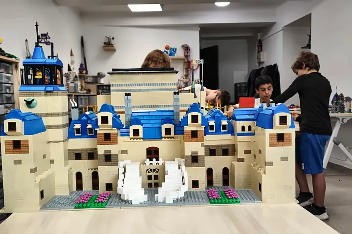 Grand château fort à toits bleus en briques LEGO®, avec tour d'horloge et escalier blanc, devant les participants du stage